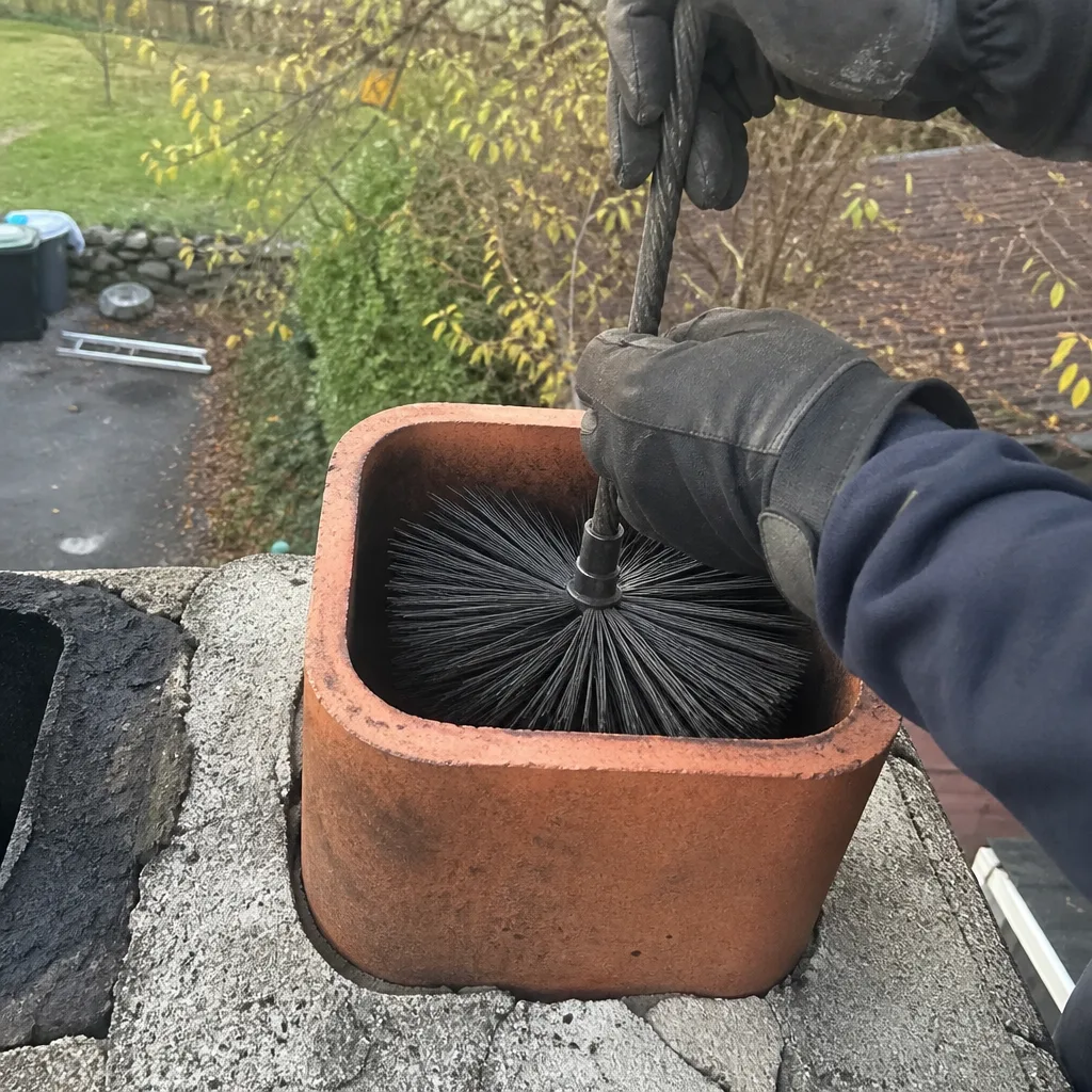 Professional chimney sweep cleaning a residential chimney stack with a brush